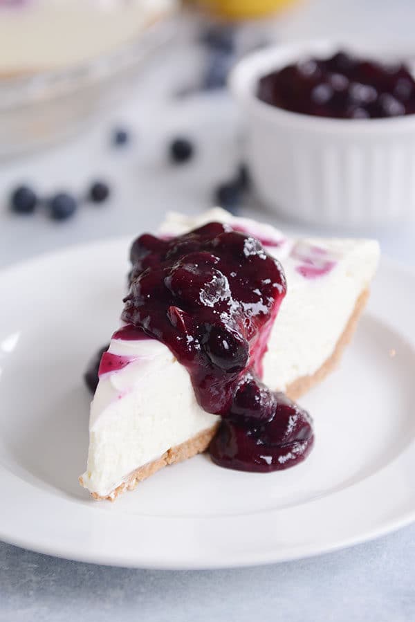 A slice of cheesecake topped with blueberry sauce on a white plate.