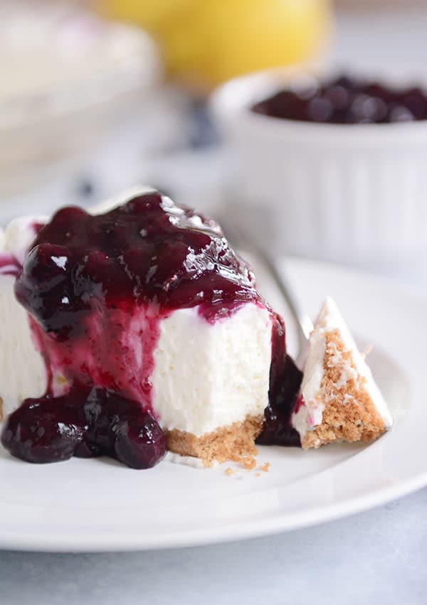 A fork taking a bite out of a slice of cheesecake that is topped with blueberry sauce.