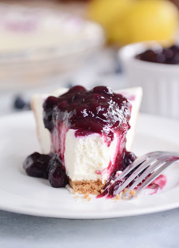 A slice of lemon cheesecake topped with blueberry sauce and one bite taken out on a white plate