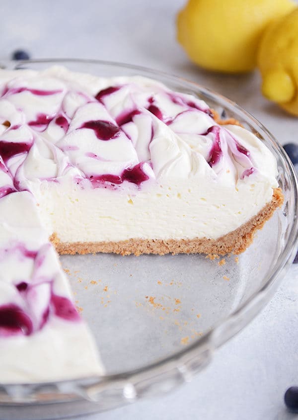 A large slice cut out of a graham cracker crust cheesecake with a blueberry swirl on top.