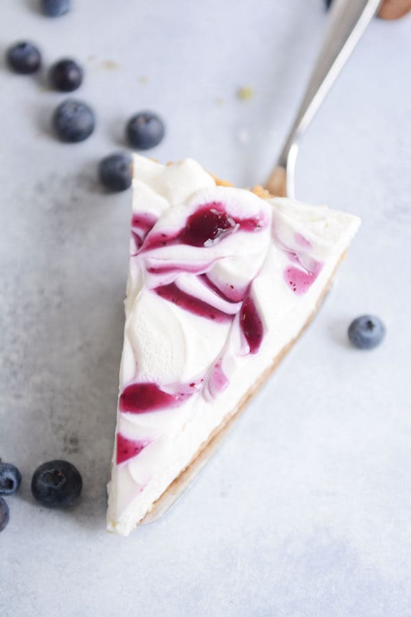 A slice of cheesecake with a swirl of blueberry sauce on top sitting on a fork.