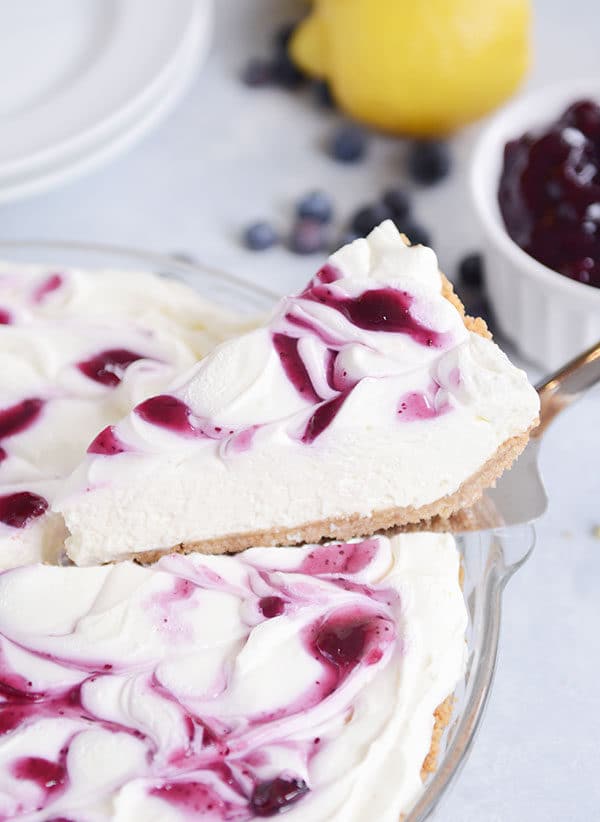 A slice of blueberry-swirled lemon cheesecake getting taken out of the a pie dish of the rest of the cheesecake.