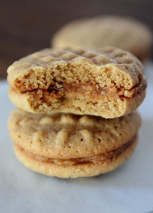 Two stacked homemade nutter butter cookies, with the top cookie with a bite taken out, on a piece of parchment paper.