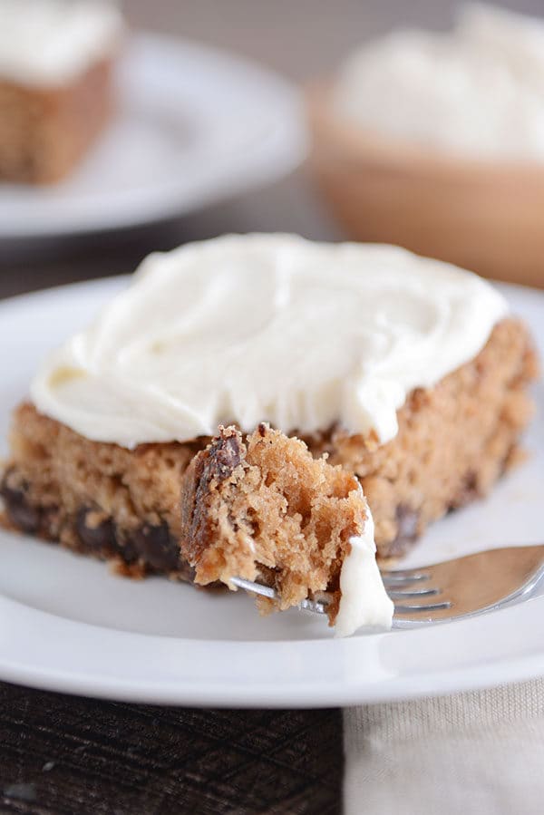 A fork taking a bite out of a piece of oatmeal chocolate chip cake with cream cheese frosting.