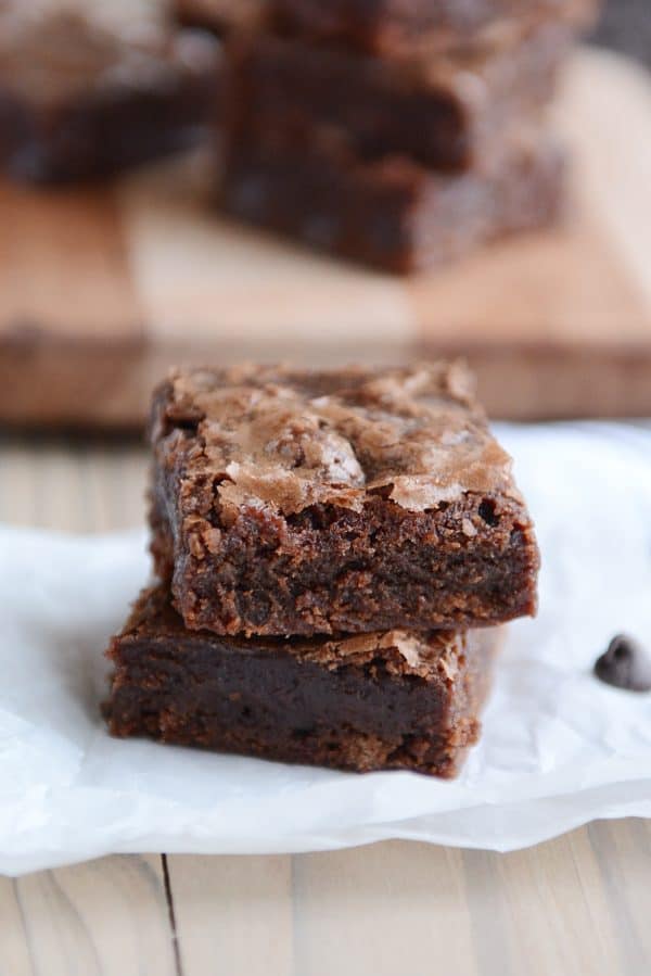 Two chocolate brownies stacked on top of each other on a piece of parchment paper. 