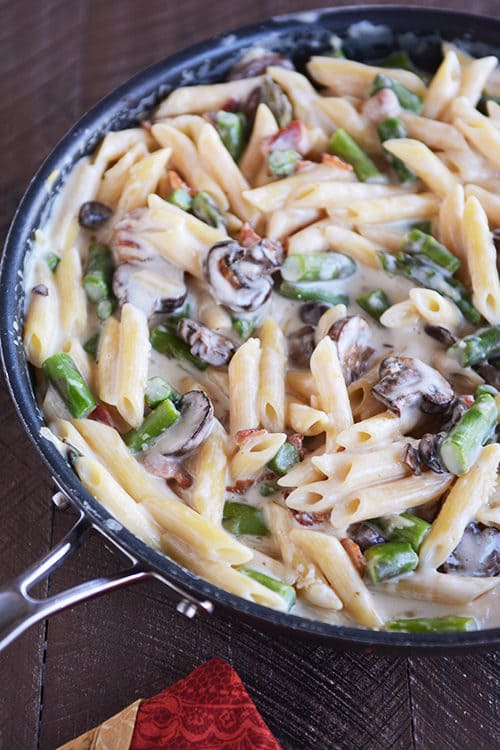Top view of a skillet full of creamy bacon, mushroom, and asparagus pasta.