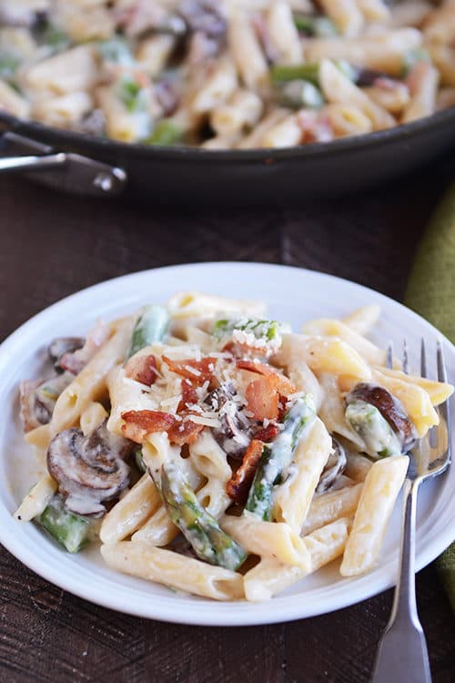 A white plate with creamy asparagus, bacon, and mushroom pasta.