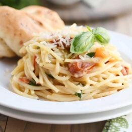 One pot creamy tomato basil pasta on white plate with parmesan breadstick.