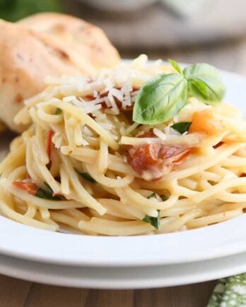 One pot creamy tomato basil pasta on white plate with parmesan breadstick.