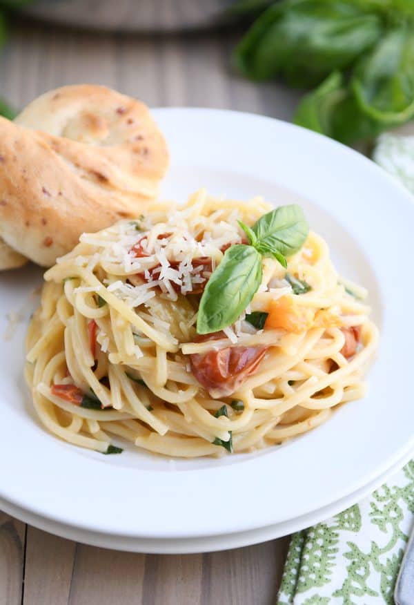 One pot creamy tomato basil pasta on white plate with parmesan breadstick.