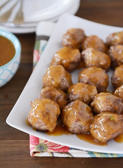 A white platter with cooked meatballs covered in an orange glaze. 