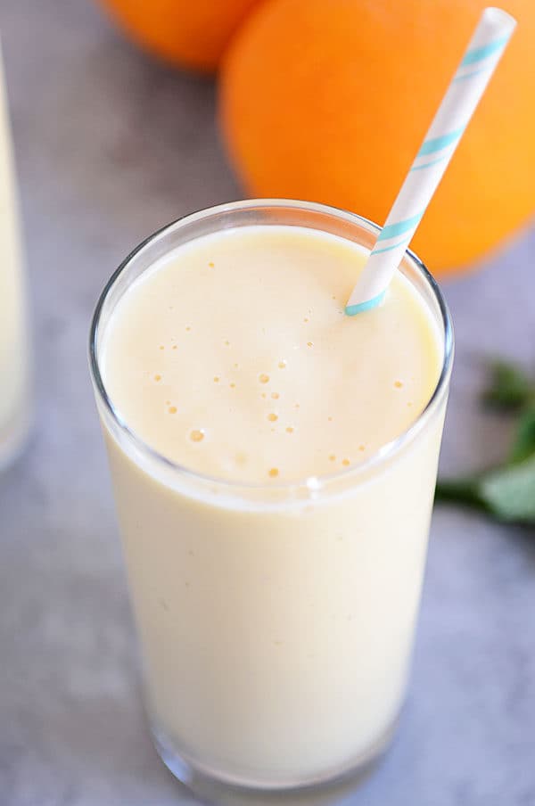 Tall glass cup of orange smoothie with a straw sticking out.