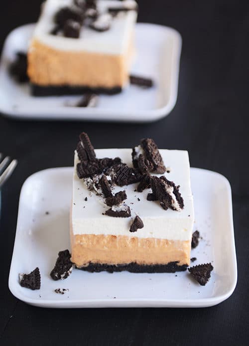 Squares of pumpkin cheesecake Oreo bars topped with chopped Oreo's on small white plates. 
