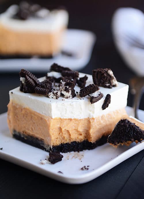 A pumpkin cheesecake bar with an Oreo crust and a bite taken out on a white plate.