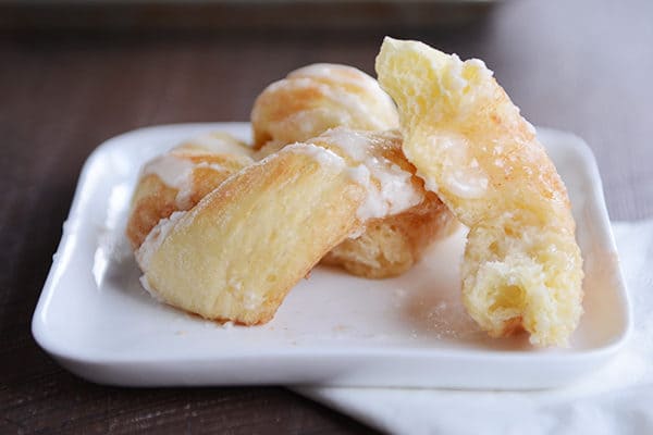 A cinnamon and sugar glazed twist with a piece ripped off on a white plate.