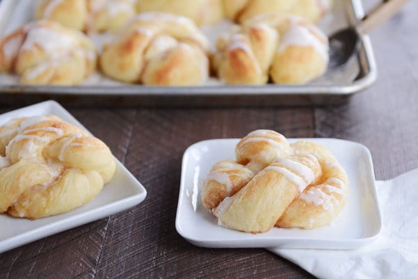 Glazed cinnamon and sugar twists on white plates with a pan of more twists behind them. 