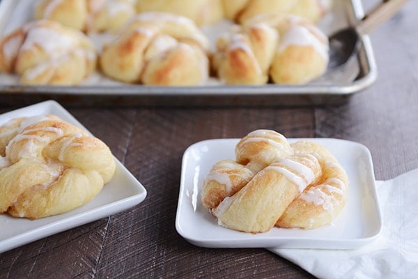 frosting drizzled cinnamon twists on small white plates with a pan of other twists behind it