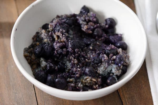 A white bowl full of blueberry filled cooked steel cut oats. 