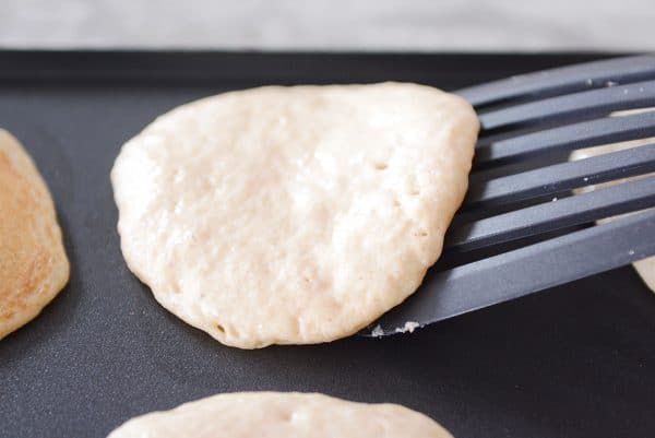 A spatula flipping a half-cooked pancake on a griddle. 