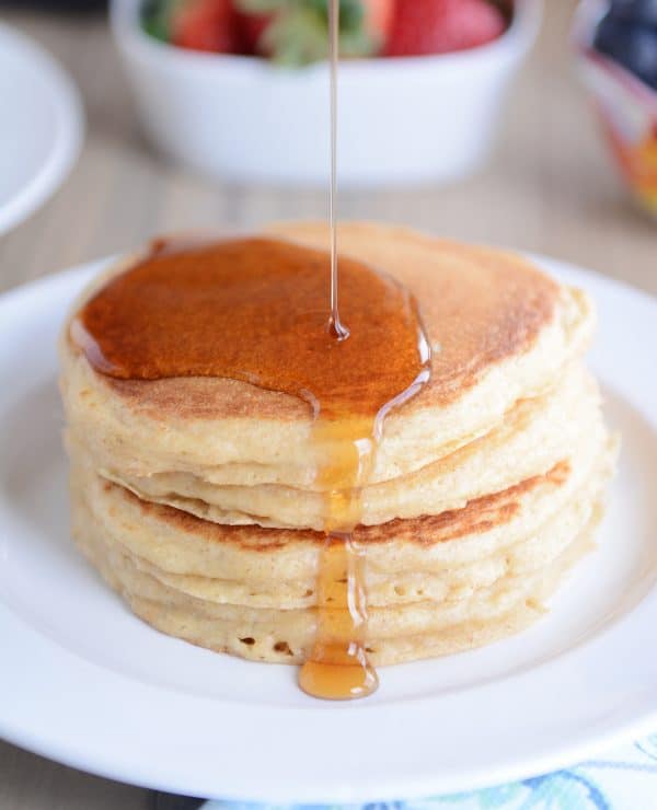 A stack of pancakes getting syrup poured over them. 