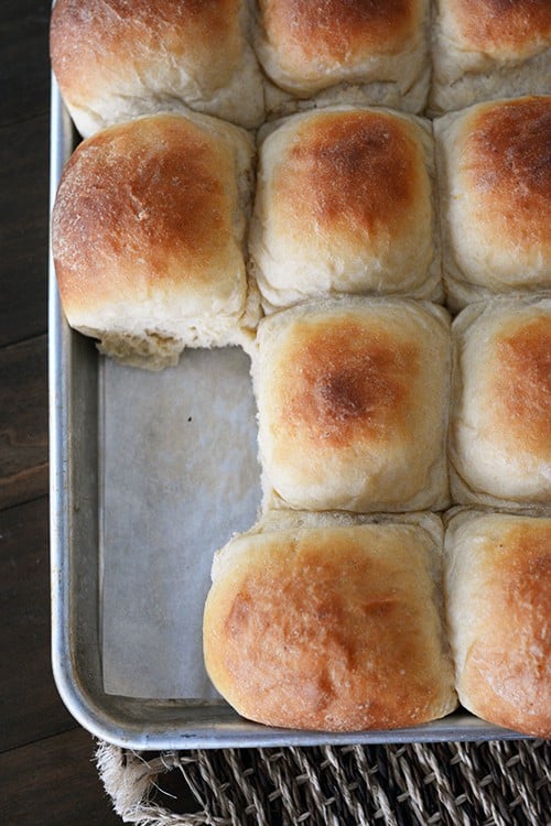 Top view of a cookie sheet full of golden brown rolls with a few missing.