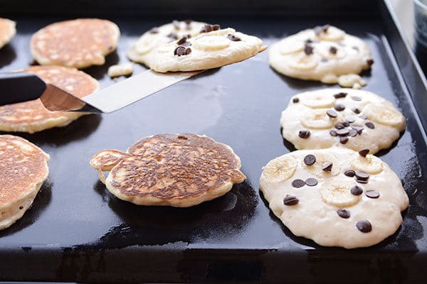 Chocolate chip pancakes getting cooked on a griddle.