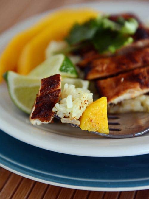 Slices of grilled chicken, mango, lime, and rice on a white plate. 