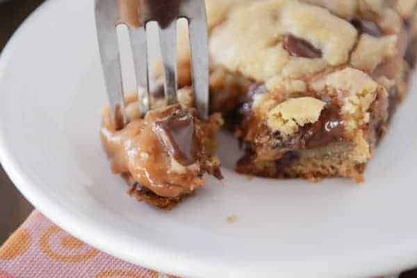 Fork taking a bite out of a peanut butter caramel bar on a white plate.