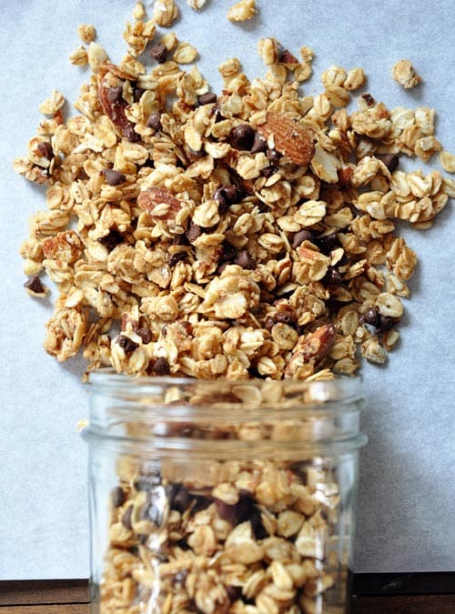 A mason jar spilling out peanut butter granola onto a piece of parchment. 