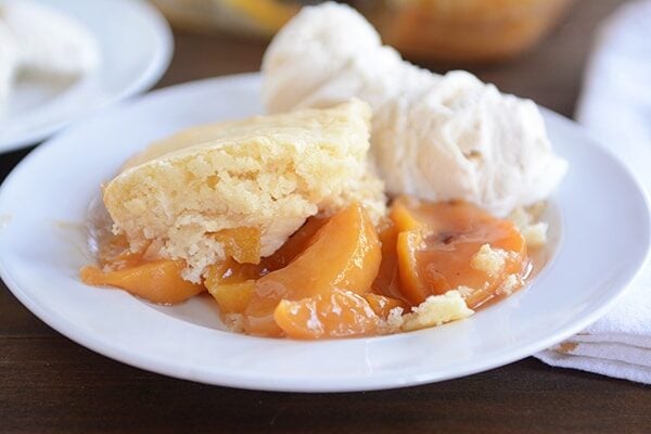 A large serving of classic peach cobbler and two scoops of vanilla ice cream on a white plate.