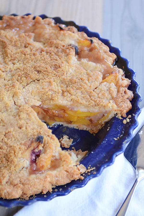A peach pie in a blue pie dish with one slice taken out.