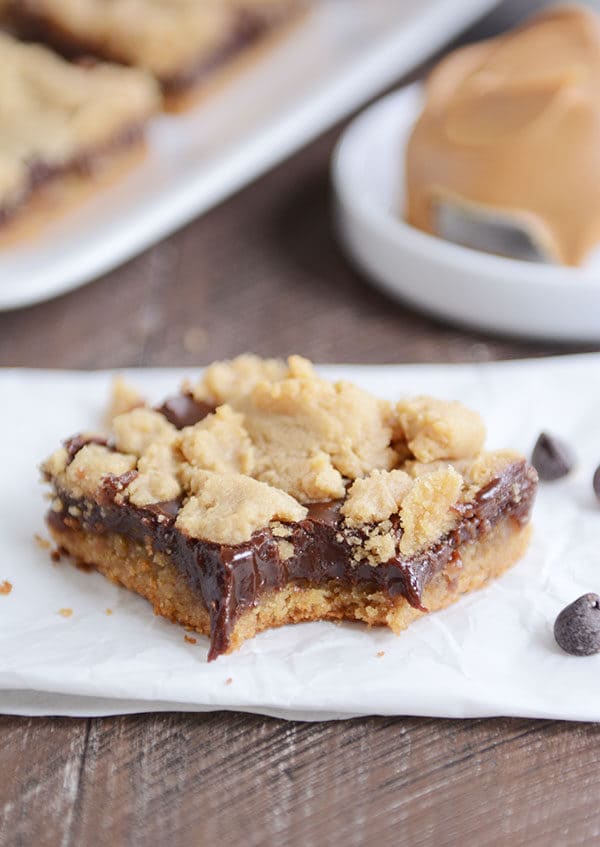 A peanut butter fudge bar with a bite taken out on a piece of parchment.