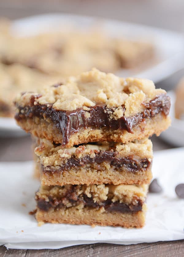 Three layered peanut butter fudge bars stacked on top of each with with a bite taken out of the top bar.