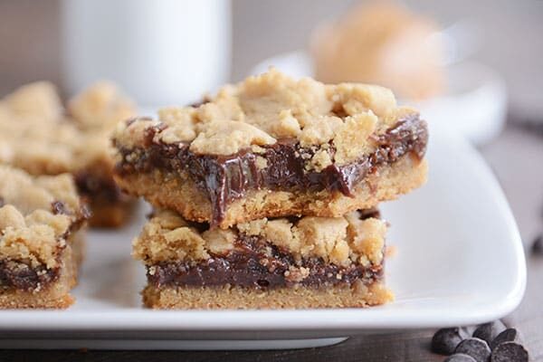 A white tray of layered peanut butter and fudge bars with a bite taken out of the top bar.