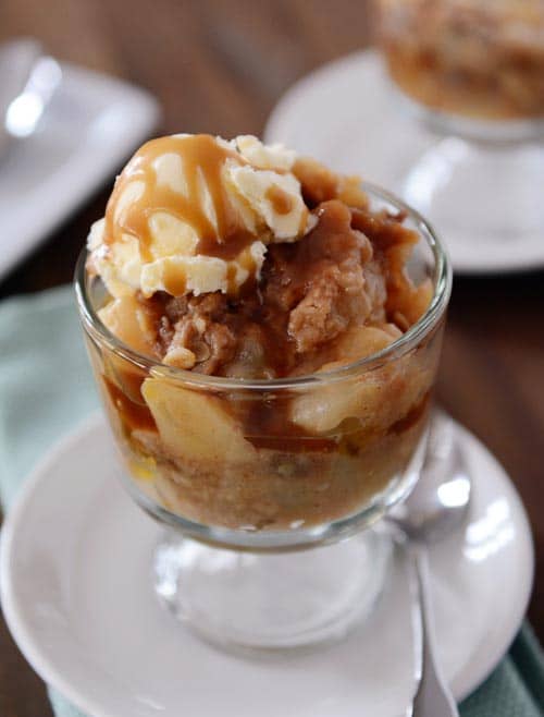 A glass goblet of caramel pear crisp and a scoop of vanilla ice cream.