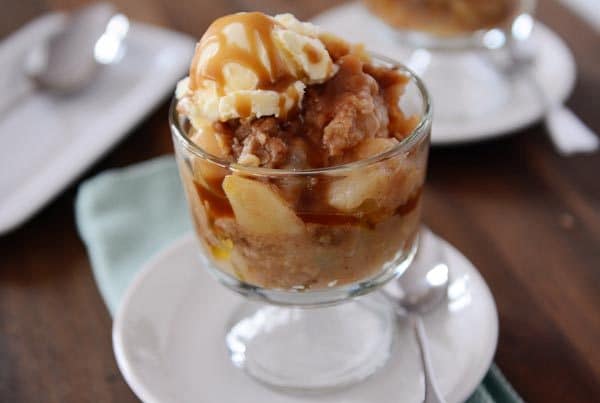 Glass goblet of pear caramel crisp with a scoop of ice cream and caramel on top.