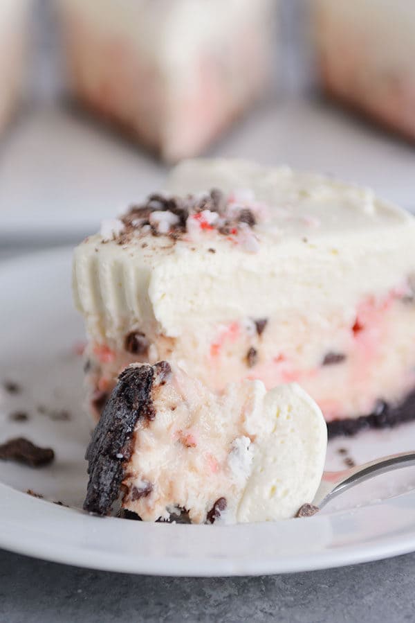 A fork taking a bite out of a slice of layered peppermint white chocolate cheesecake.