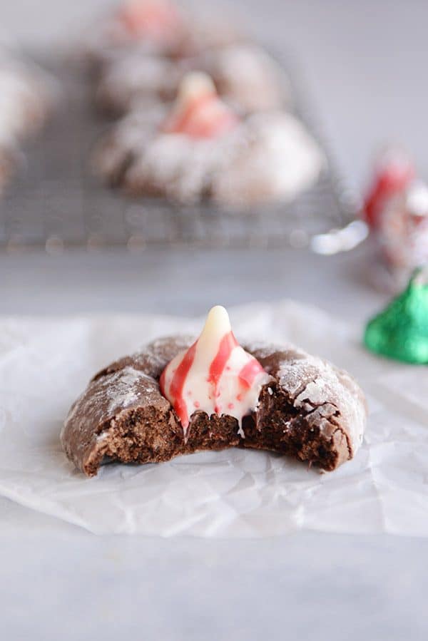 A chocolate blossom cookie with a bite taken out on a piece of parchment.