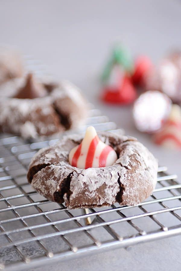 A chocolate peppermint blossom cookie with a striped Hershey kiss on a cooling rack.