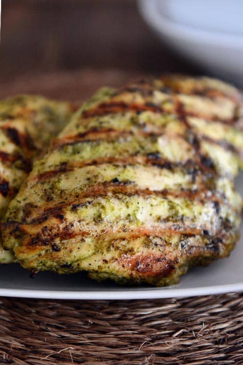 A white platter with a large pesto coated grilled chicken breast. 