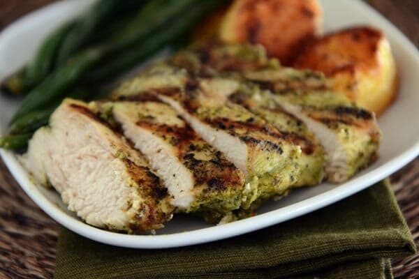 A pesto grilled chicken breast cut into big slices on a white plate. 