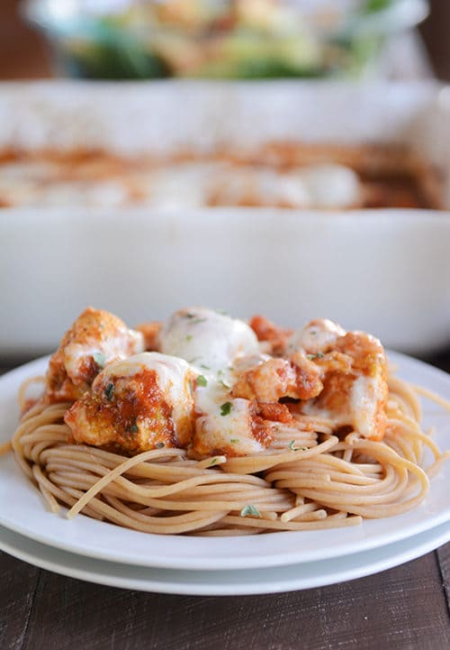 A white plate of cooked spaghetti topped with cheesy marinara chicken.