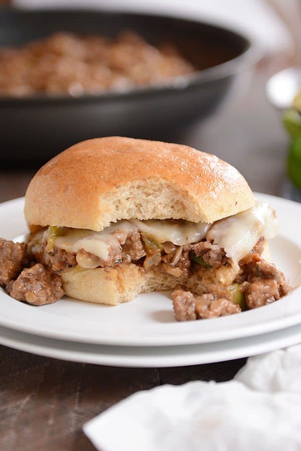 A white plate with a philly cheesesteak sloppy joe with a bite taken out.