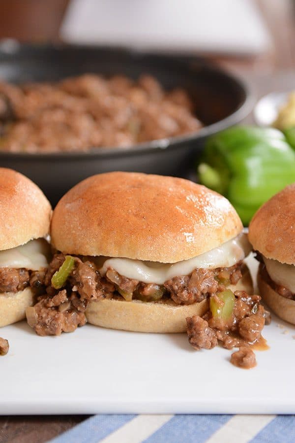 A philly cheesesteak sloppy joe on a golden brown bun, with some of the mixture spilling out onto the plate.
