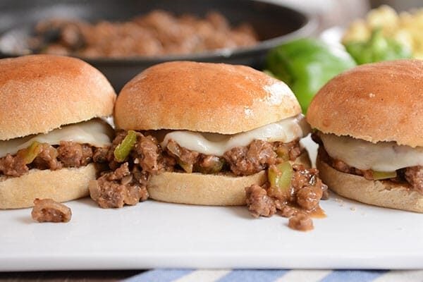 Three Philly cheesesteak sloppy joe's lined up on a white cutting board.