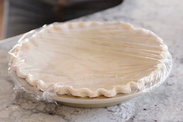 An uncooked pie crust with a crimped edge, covered in saran wrap.