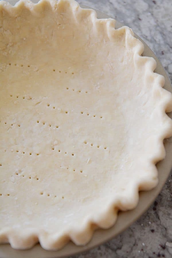 An uncooked, crimped-edge pie crust, with fork holes in the bottom.