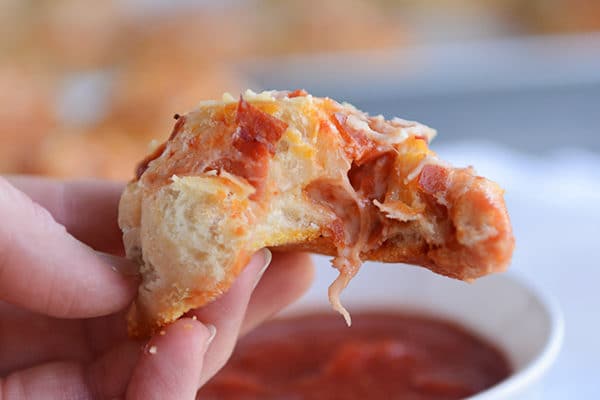 A pepperoni pizza roll with a bite taken out, being held over a bowl of marinara sauce.