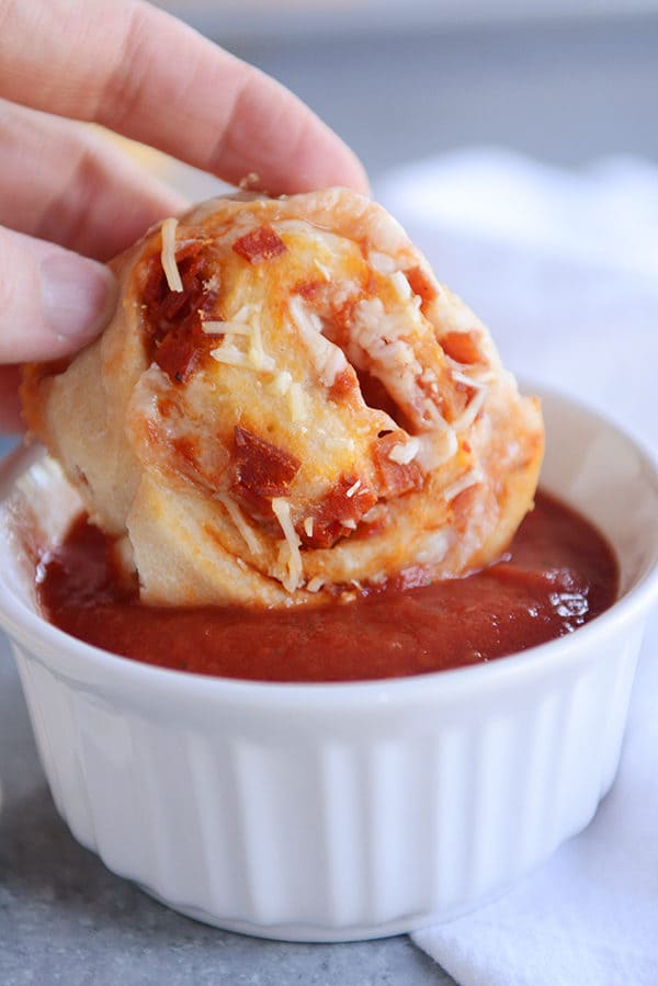 A pepperoni pizza roll being dipped in a bowl of marinara sauce. 