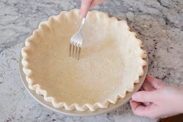 A fork poking holes in the bottom of an uncooked pie crust.